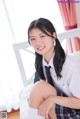 A young woman in a school uniform sitting on a bed.